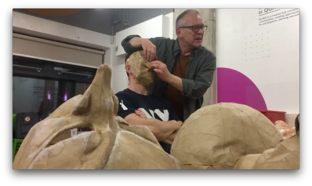 A mask maker has wrapped another man's head in tape to create a mask as part of the Ancestories project