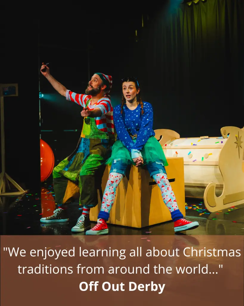Two actors in christmas clothes sit in front of a sleigh on stage during a performance of Merry Elwin: The Adventurous Elf