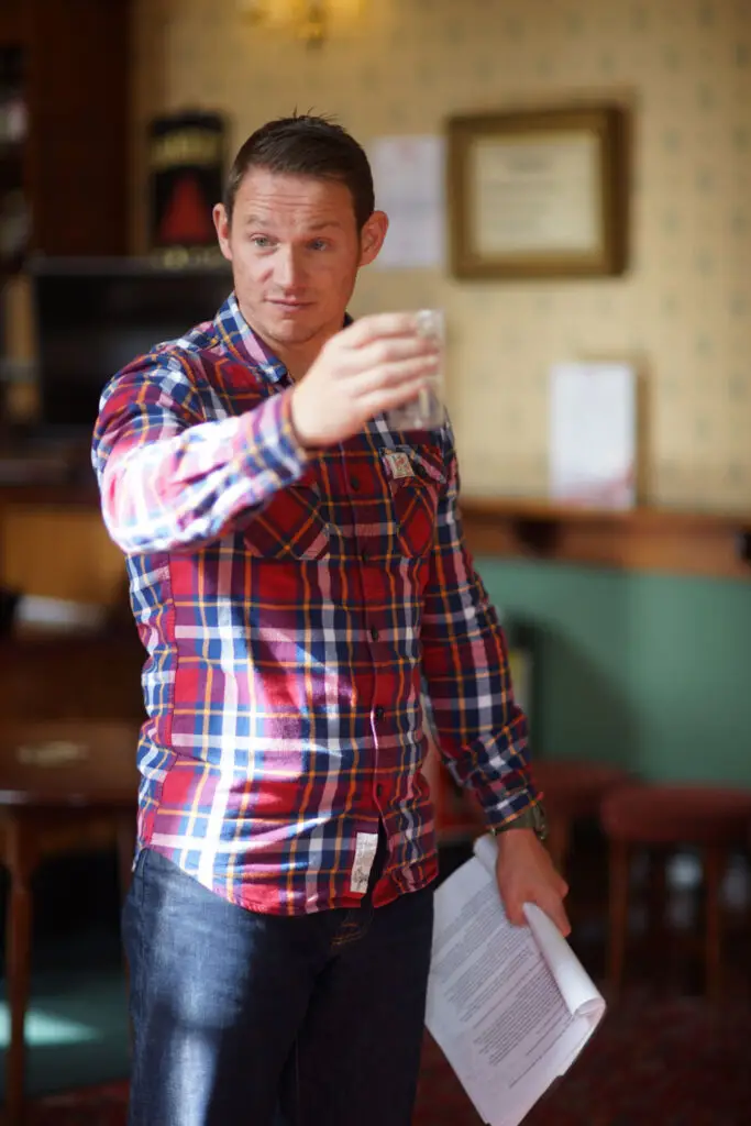 Paul holds out a plastic cup of liquid, a prop, as he rehearses Paul's Ball