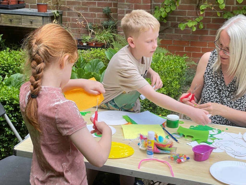 Two children and a woman cut colourful paper and use paper plates to make masks as part of the Animates project with Paul Broesmith